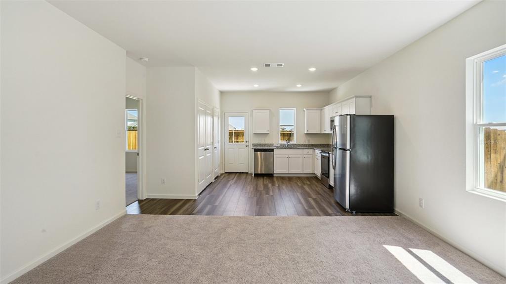A kitchen with white cabinets and stainless steel appliances opens into a carpeted living area — 5859 KALAMATA DRIVE, POLK CITY, FL