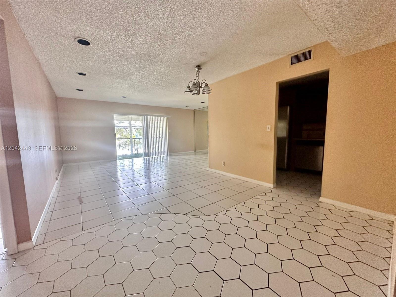 An open living area features white hexagonal floor tiles, large square tiles, and a sliding glass door — 3360 Spanish Moss Ter # 206, Lauderhill FL 33319, LAUDERHILL, FL