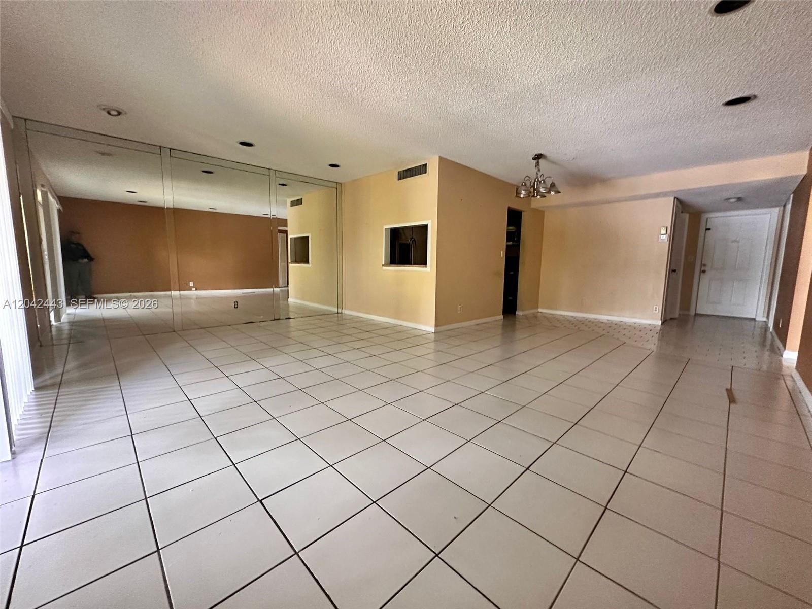 An empty room features white tiled floors, mirrored walls, and a pass-through window — 3360 Spanish Moss Ter # 206, Lauderhill FL 33319, LAUDERHILL, FL