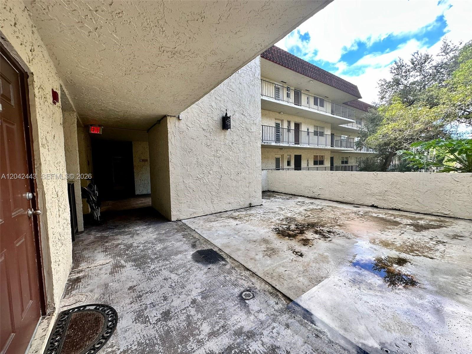 A weathered concrete patio sits beneath a building overhang next to a brown door — 3360 Spanish Moss Ter # 206, Lauderhill FL 33319, LAUDERHILL, FL