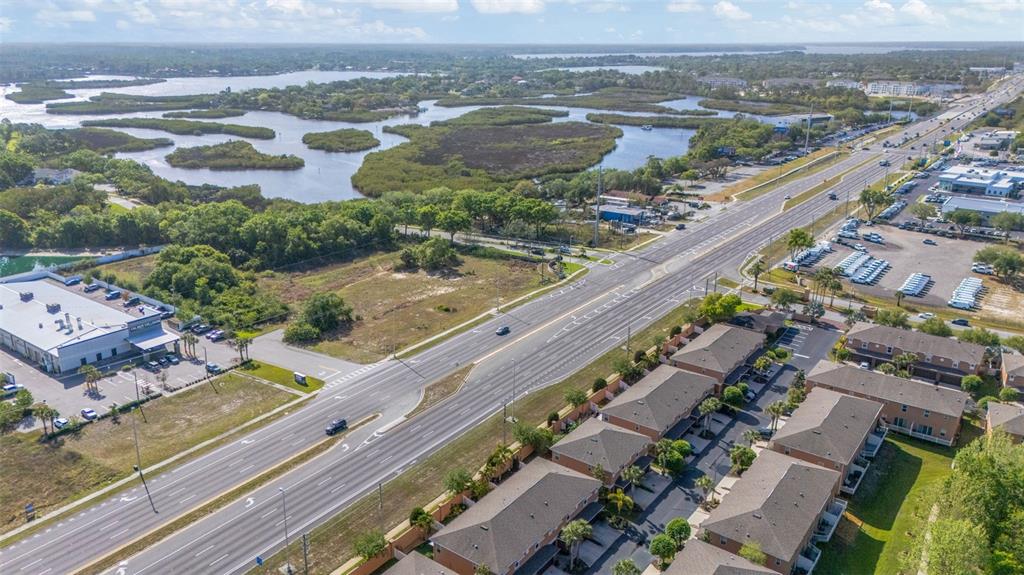An aerial view shows a multi-lane highway running past a residential complex and wetlands — 1819 SOMMARIE WAY, TARPON SPRINGS, FL