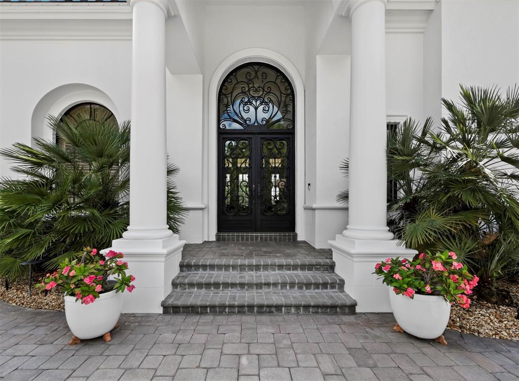 A white house entrance features a black arched double door, columns, and two potted plants — 3129 FOUNDERS CLUB DRIVE, SARASOTA, FL