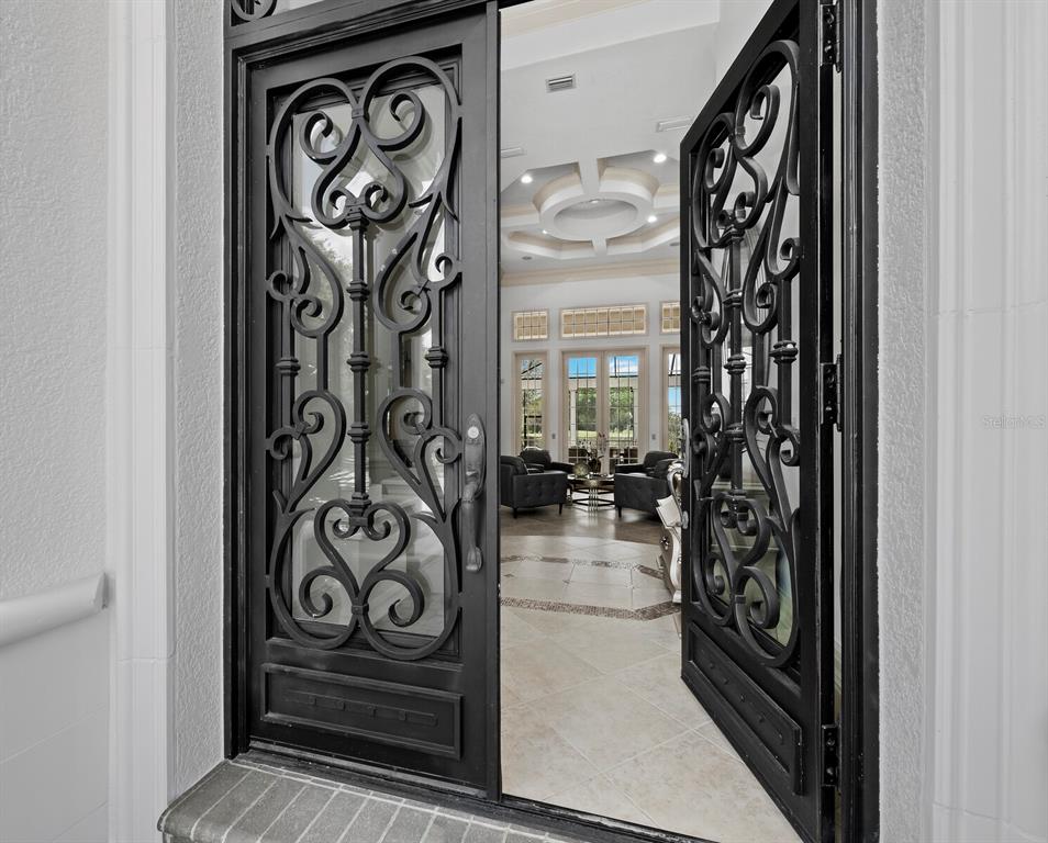 An open wrought iron double door reveals a tiled foyer and a living room beyond — 3129 FOUNDERS CLUB DRIVE, SARASOTA, FL