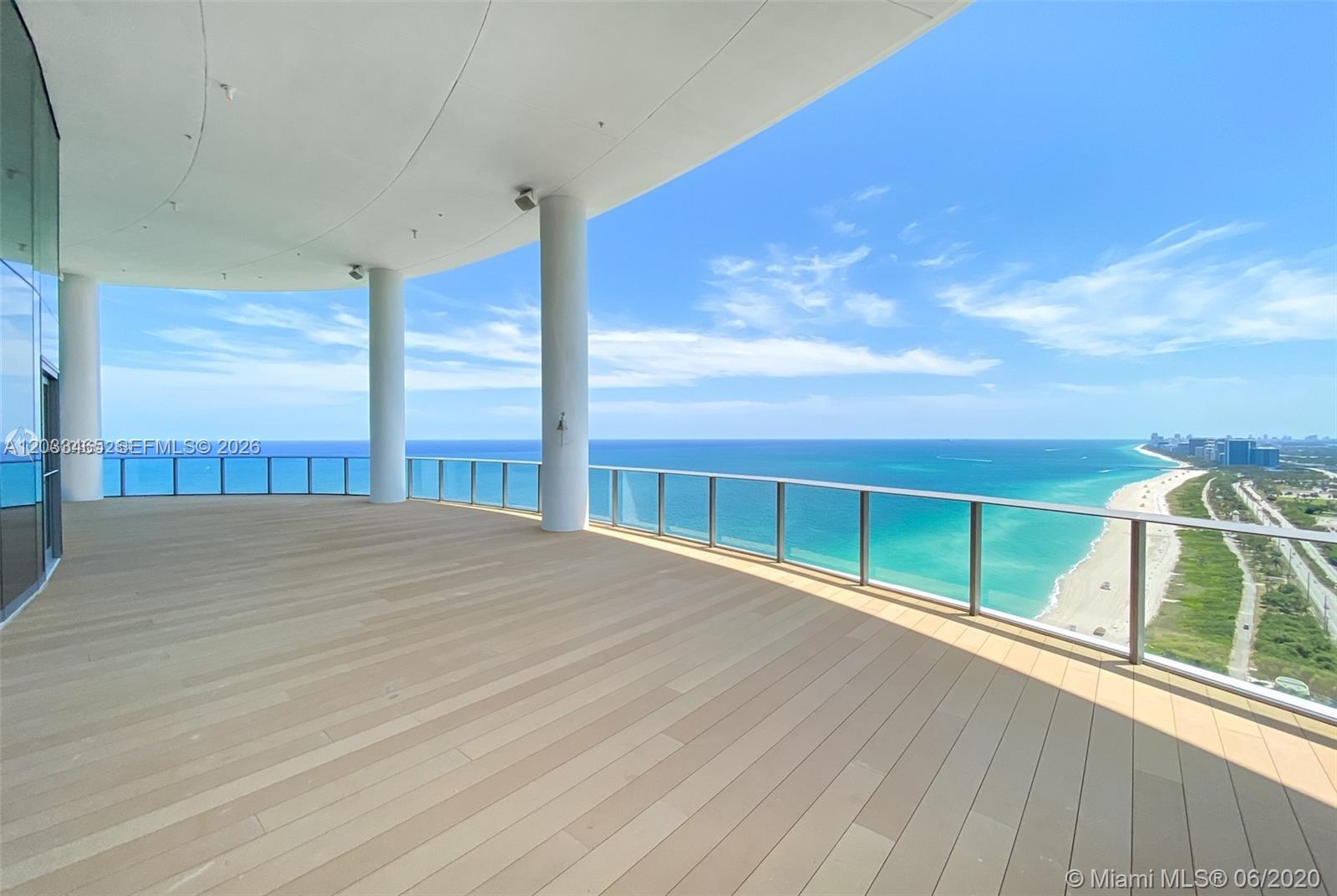 A spacious, curved balcony features light wood flooring, glass railings, and expansive ocean views — 15701 E COLLINS # 1403, Sunny Isles Beach FL 33160, SUNNY ISLES BEACH, FL