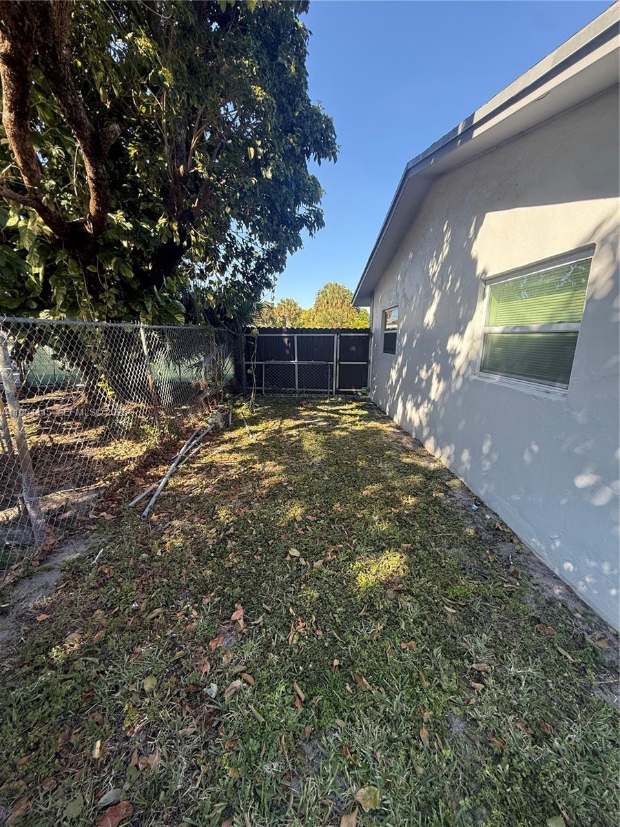 A narrow side yard features a chain-link fence, a tree, and a light-colored house wall — 310 NE 38th St, Deerfield Beach FL 33064, DEERFIELD BEACH, FL