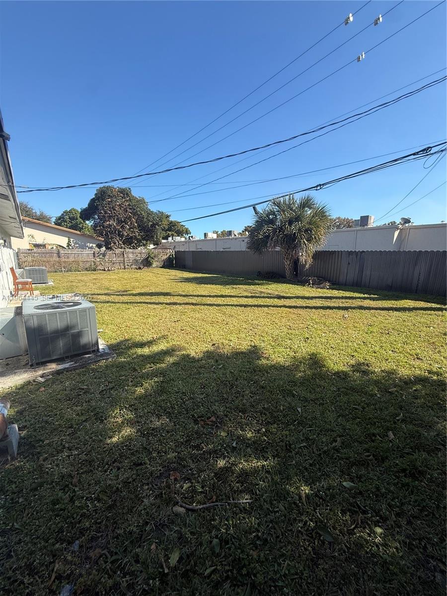 A grassy backyard features a central palm tree, a wooden fence, and an air conditioning unit — 310 NE 38th St, Deerfield Beach FL 33064, DEERFIELD BEACH, FL