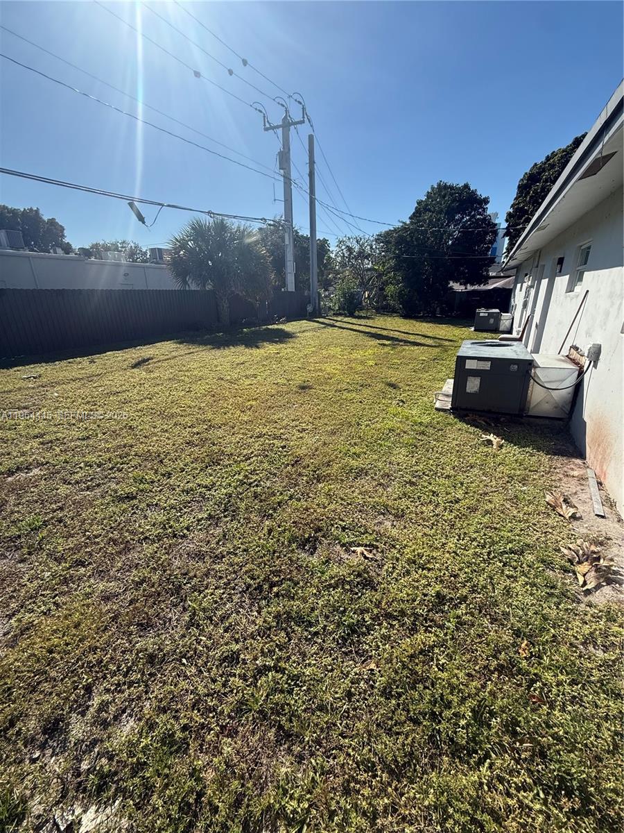 A grassy backyard features a central air conditioning unit against the side of a house — 310 NE 38th St, Deerfield Beach FL 33064, DEERFIELD BEACH, FL