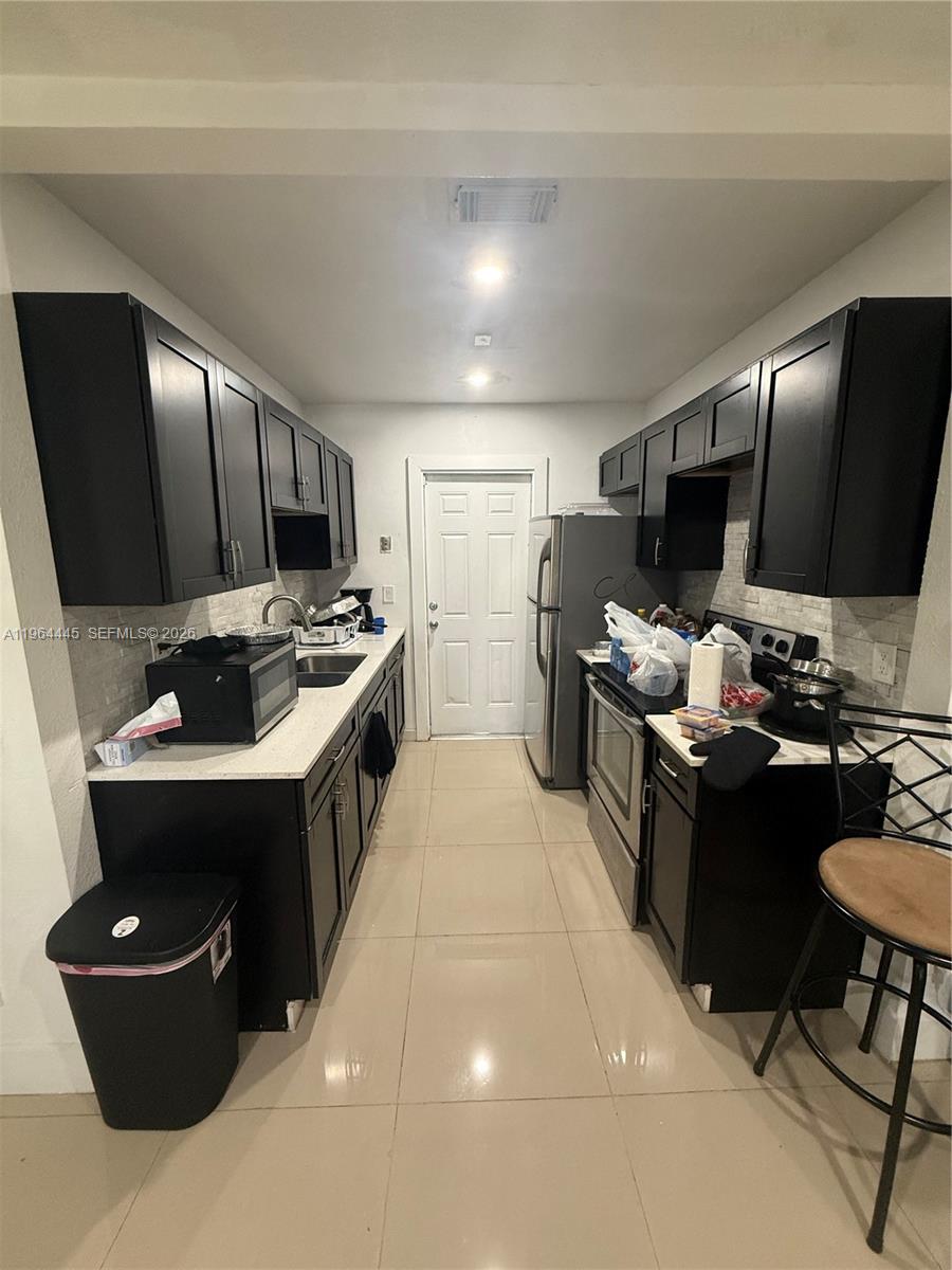 A galley-style kitchen features dark cabinetry, light countertops, stainless steel appliances, and tiled flooring — 310 NE 38th St, Deerfield Beach FL 33064, DEERFIELD BEACH, FL