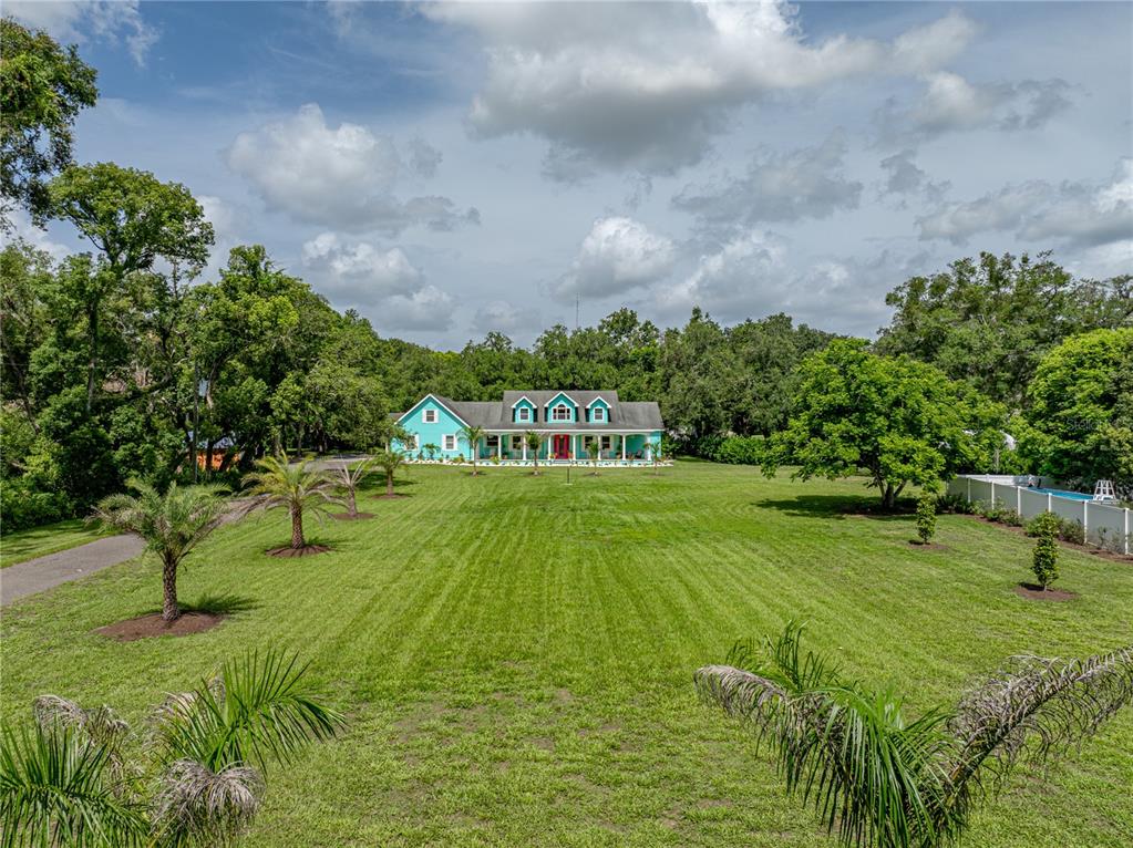 A teal house with a red front door sits at the end of a large lawn — 7427 20TH STREET, ZEPHYRHILLS, FL