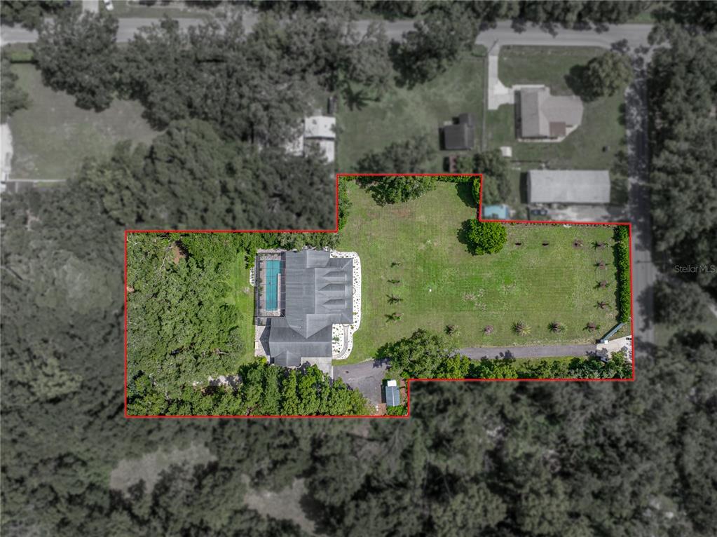An aerial view shows a house with a pool on a large, partially wooded lot — 7427 20TH STREET, ZEPHYRHILLS, FL