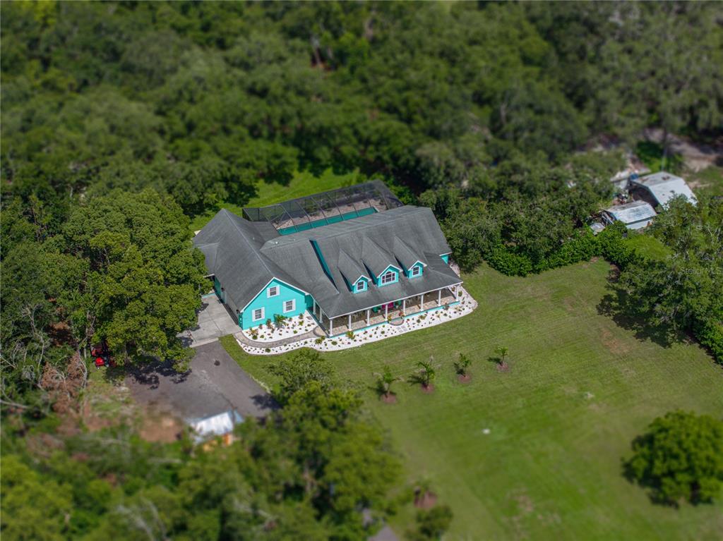 An aerial view shows a teal house with a screened pool and a large lawn — 7427 20TH STREET, ZEPHYRHILLS, FL
