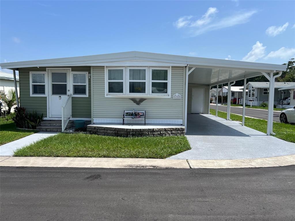 A single-story manufactured home features light green siding, a front porch, and an attached carport — 11300 124TH AVENUE UNIT 122, LARGO, FL