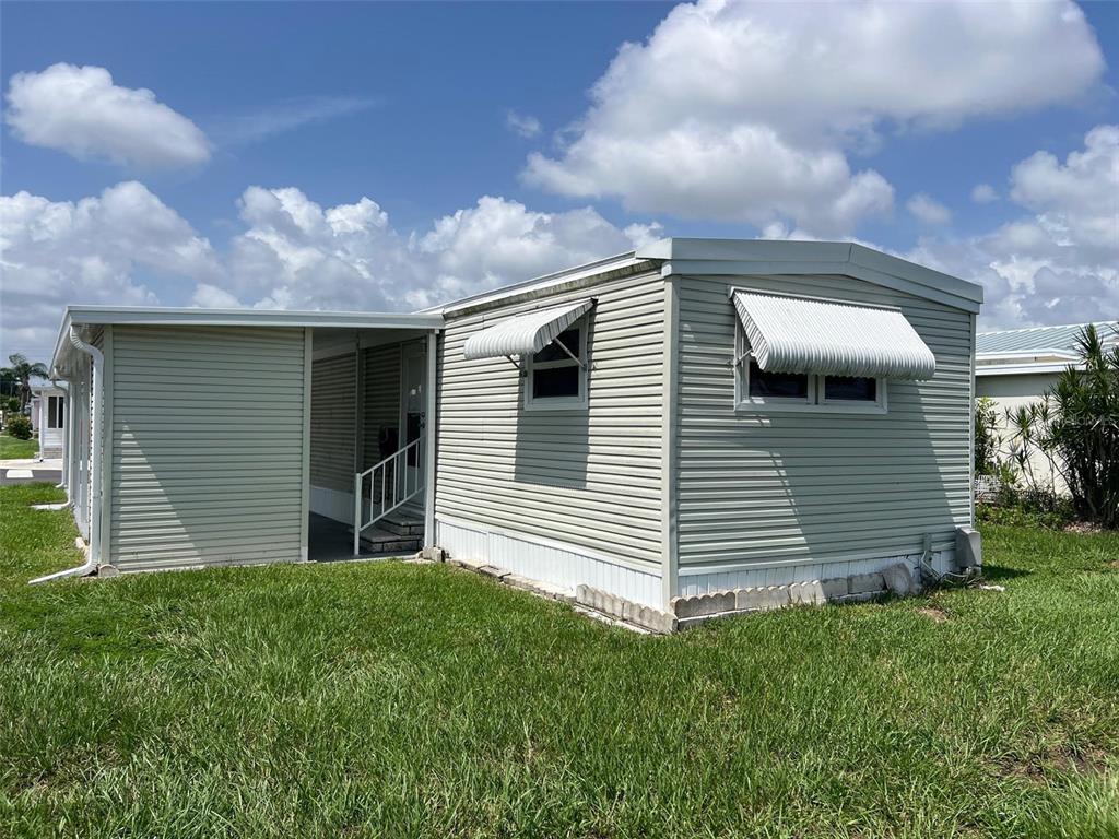 A light-colored mobile home with horizontal siding, metal window awnings, and a covered entryway — 11300 124TH AVENUE UNIT 122, LARGO, FL