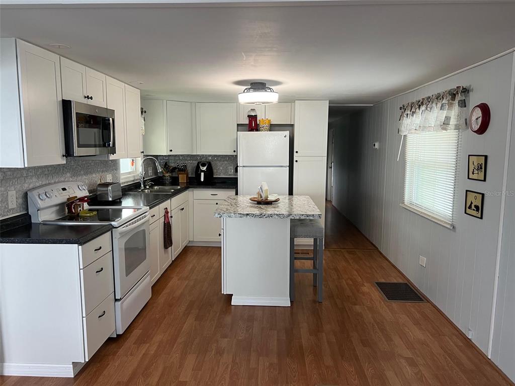 A kitchen features white cabinets, a granite-topped island, and wood-look flooring — 11300 124TH AVENUE UNIT 122, LARGO, FL
