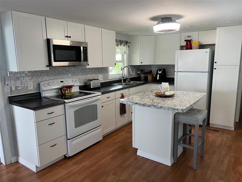 A kitchen features white cabinets, granite countertops, a white stove, and a central island — 11300 124TH AVENUE UNIT 122, LARGO, FL
