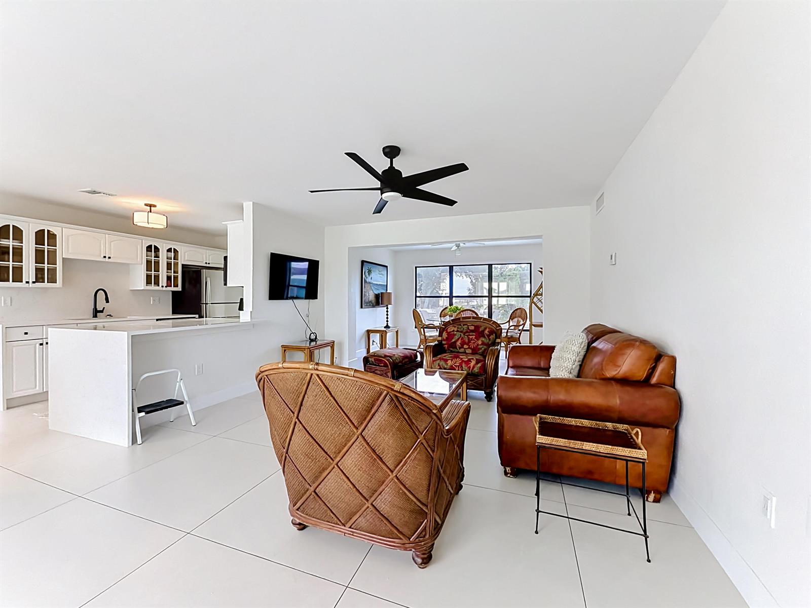 An open-concept living room features a leather sofa, wicker chairs, and a white kitchen — 3234 Daytona Drive, Punta Gorda FL 33983, PUNTA GORDA, FL