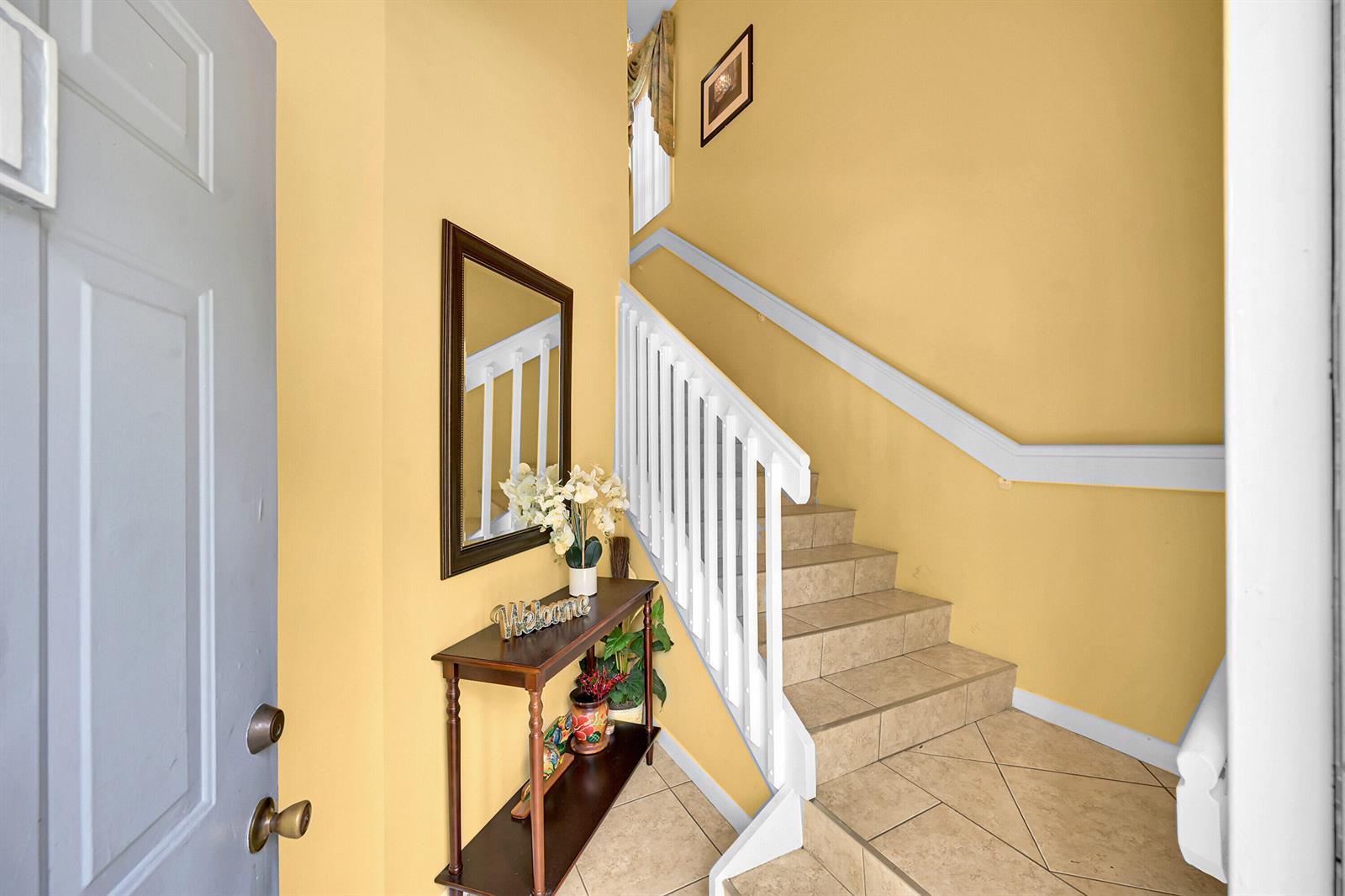 An entryway features yellow walls, a wooden console table with a mirror, and tiled stairs — 5379 Verona Drive # H, Boynton Beach FL 33437, BOYNTON BEACH, FL