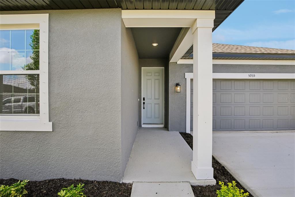 The exterior of a house features a gray stucco facade, a covered entryway, and a garage — 5935 FRESH FLORA DRIVE, WIMAUMA, FL