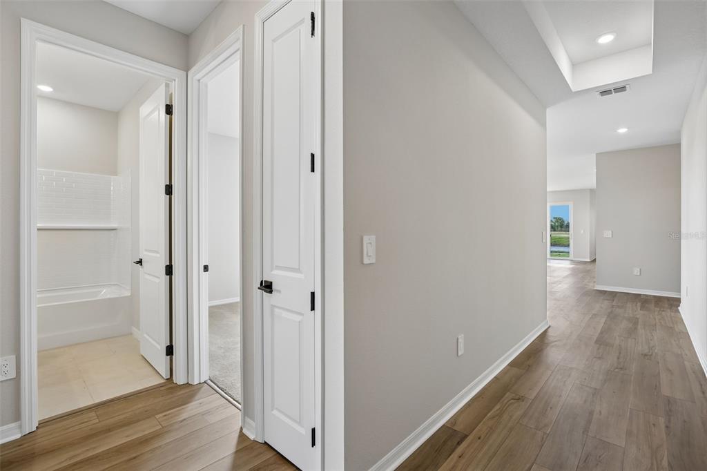 A hallway with wood-look flooring leads past a bathroom and bedroom toward a bright living area — 5935 FRESH FLORA DRIVE, WIMAUMA, FL
