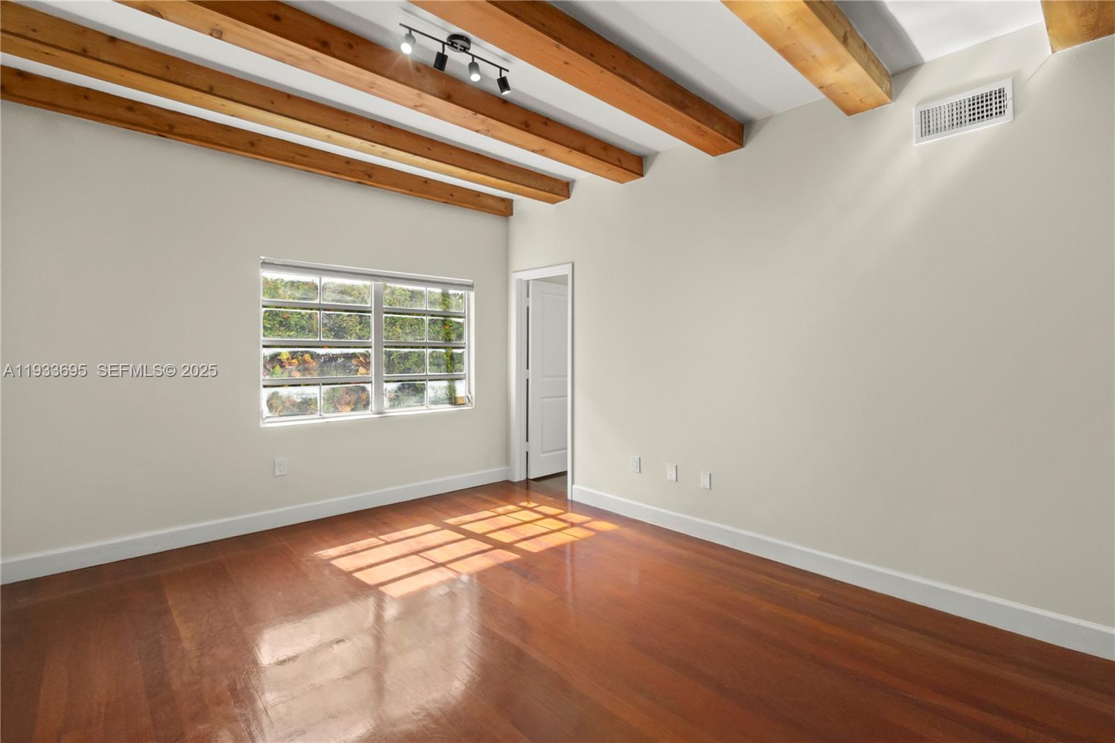 An empty room features hardwood floors, exposed wooden ceiling beams, and a multi-pane window — 1605 Euclid Ave # A1, Miami Beach FL 33139, MIAMI BEACH, FL