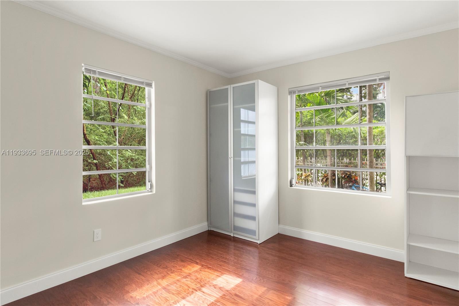A bedroom features hardwood floors, two windows, a white wardrobe, and a white bookshelf — 1605 Euclid Ave # A1, Miami Beach FL 33139, MIAMI BEACH, FL