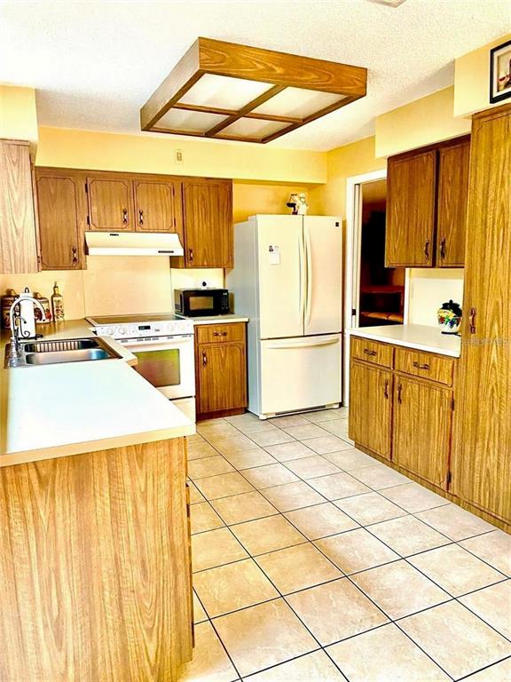 A kitchen features wood cabinets, white appliances, a tile floor, and a large light fixture — 12 WESTGABLE PLACE, PALM COAST, FL
