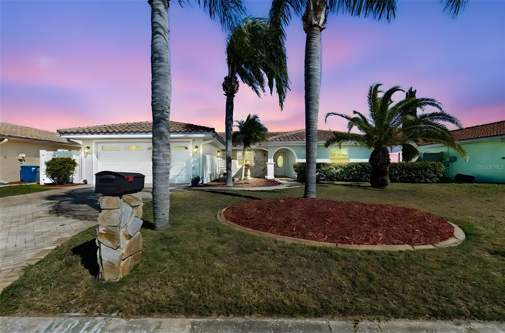 A single-story house with a two-car garage, palm trees, and a stone mailbox at sunset — 9816 SAN SEBASTIAN WAY, PORT RICHEY, FL