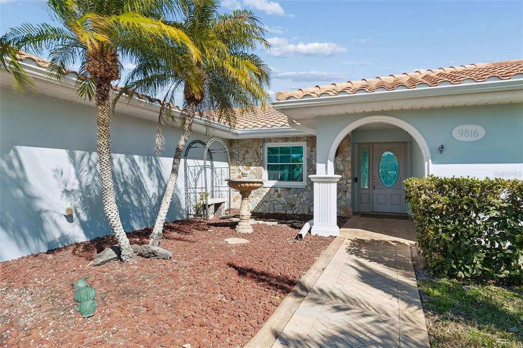 A paved walkway leads to the front entrance of a house with stone accents — 9816 SAN SEBASTIAN WAY, PORT RICHEY, FL