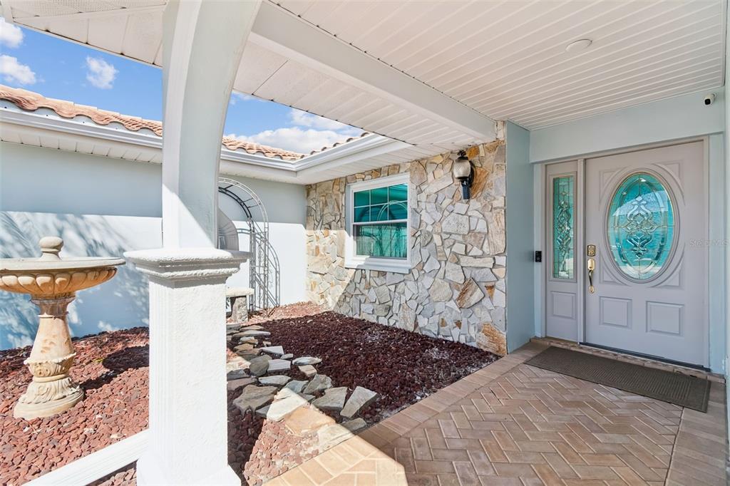 An entryway features a stone-accented wall, a paved walkway, a fountain, and a front door — 9816 SAN SEBASTIAN WAY, PORT RICHEY, FL