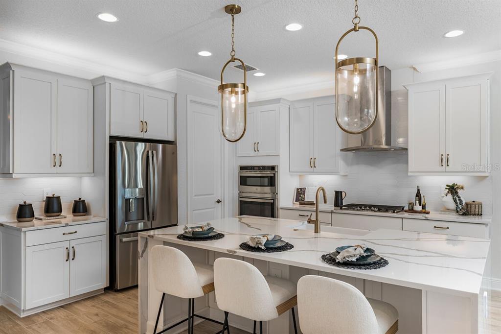 A modern kitchen features white cabinetry, a marble-topped island with seating, and gold pendant lights — 9616 VIBRANT LANE, VENICE, FL