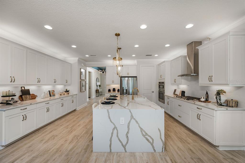 A modern kitchen features white cabinetry, a large marble-topped island, and light wood-look flooring — 9616 VIBRANT LANE, VENICE, FL