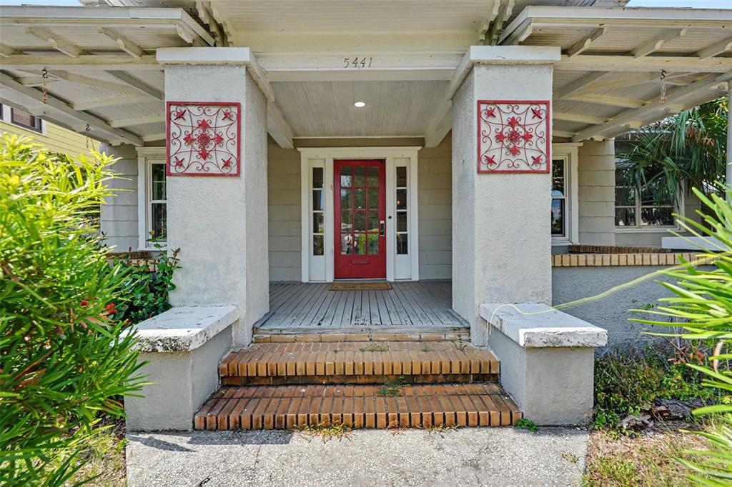 A front porch with brick steps, a red door, and decorative metal wall art — 5441 1ST AVENUE N, ST PETERSBURG, FL