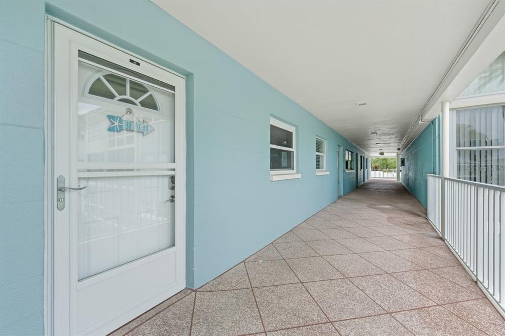 An outdoor walkway with light blue walls, tiled flooring, and a white door with a sign — 6061 2ND STREET E UNIT 45, ST PETERSBURG, FL