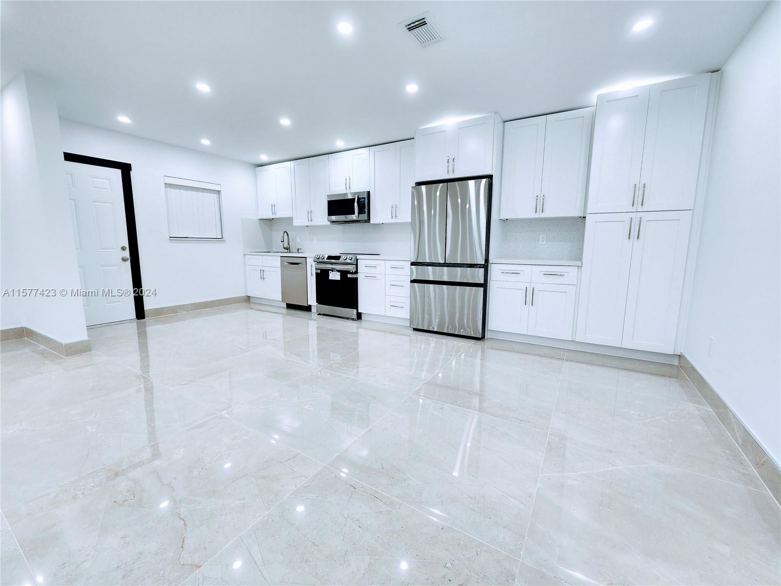 A modern kitchen features white cabinetry, stainless steel appliances, and large light-colored floor tiles — 11930 NE 19th Dr # 3, North Miami FL 33181, NORTH MIAMI, FL