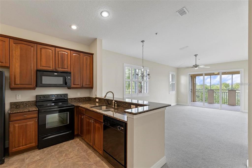 A kitchen with wood cabinets and granite countertops opens to a carpeted living area with balcony — 35 RIVERVIEW BEND S UNIT 1841, PALM COAST, FL