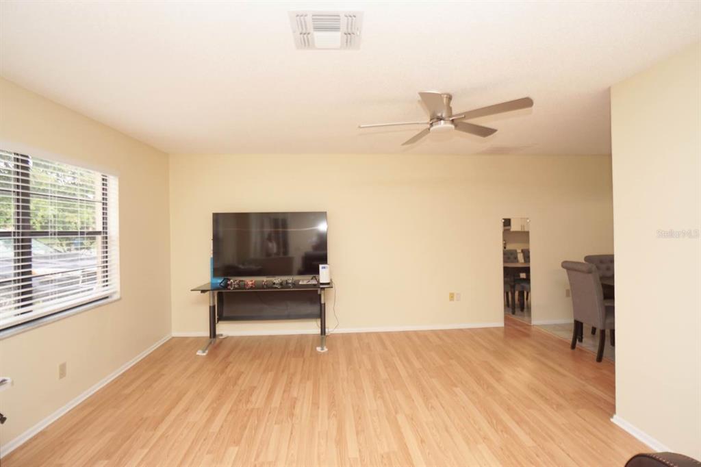 A living room with light wood flooring, a ceiling fan, and a television on a stand — 11077 LIGHTWOOD STREET, SPRING HILL, FL