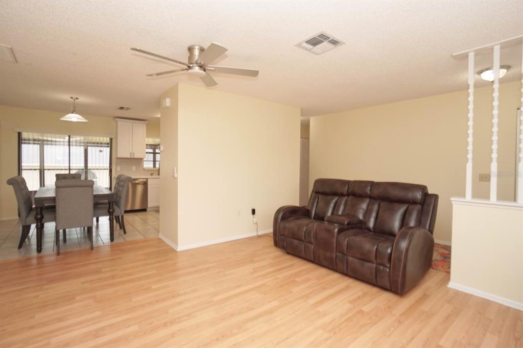 A living room with wood-look flooring and a brown leather sofa next to a dining area — 11077 LIGHTWOOD STREET, SPRING HILL, FL