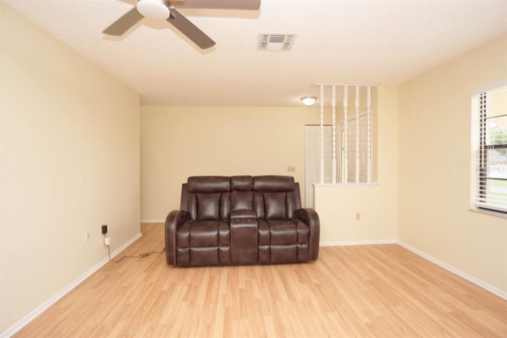 A living room with light-colored walls, wood-look flooring, a ceiling fan, and a brown sofa — 11077 LIGHTWOOD STREET, SPRING HILL, FL