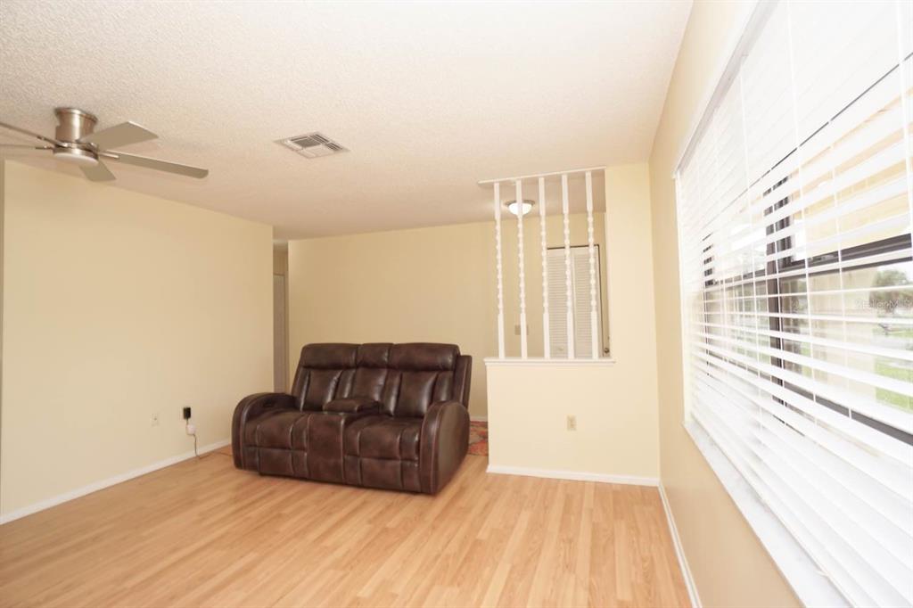 A living room with light wood flooring, a brown leather loveseat, and a decorative room divider — 11077 LIGHTWOOD STREET, SPRING HILL, FL