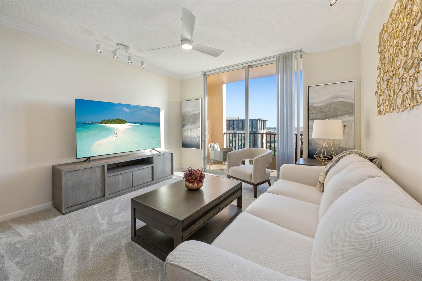 A living room features a white sofa, coffee table, television, and a balcony with views — 651 Okeechobee Boulevard # 1107, West Palm Beach FL 33401, WEST PALM BEACH, FL