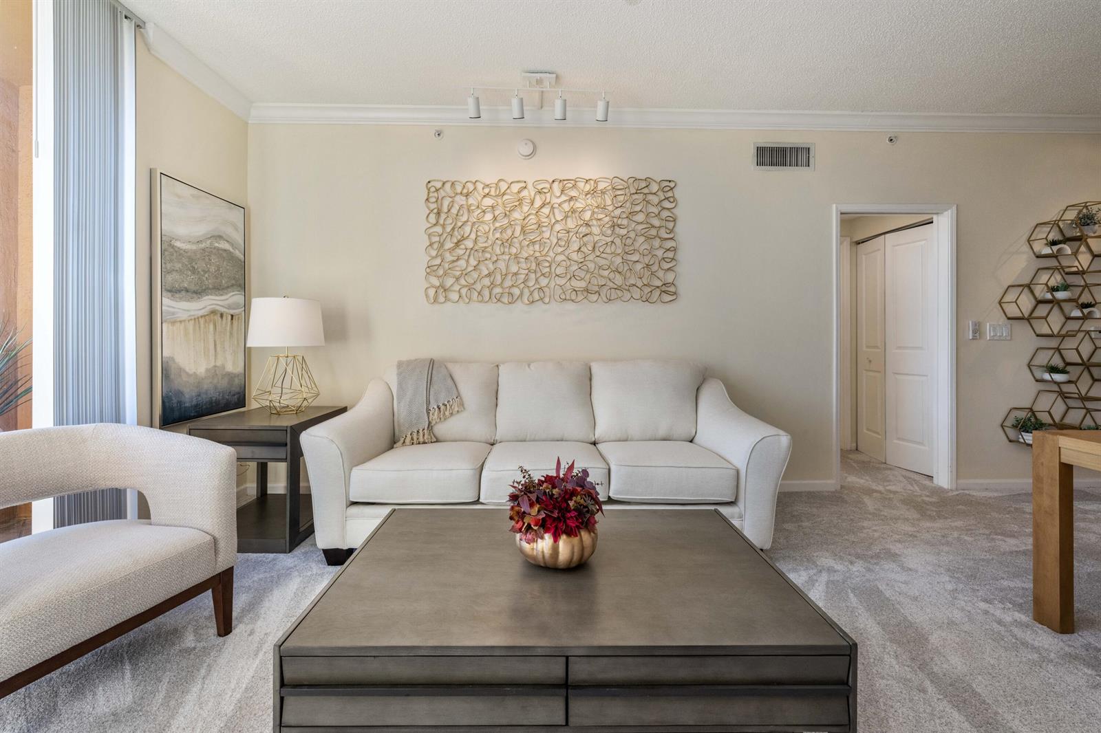 A living room features a white sofa, a square coffee table, and gold wall art — 651 Okeechobee Boulevard # 1107, West Palm Beach FL 33401, WEST PALM BEACH, FL