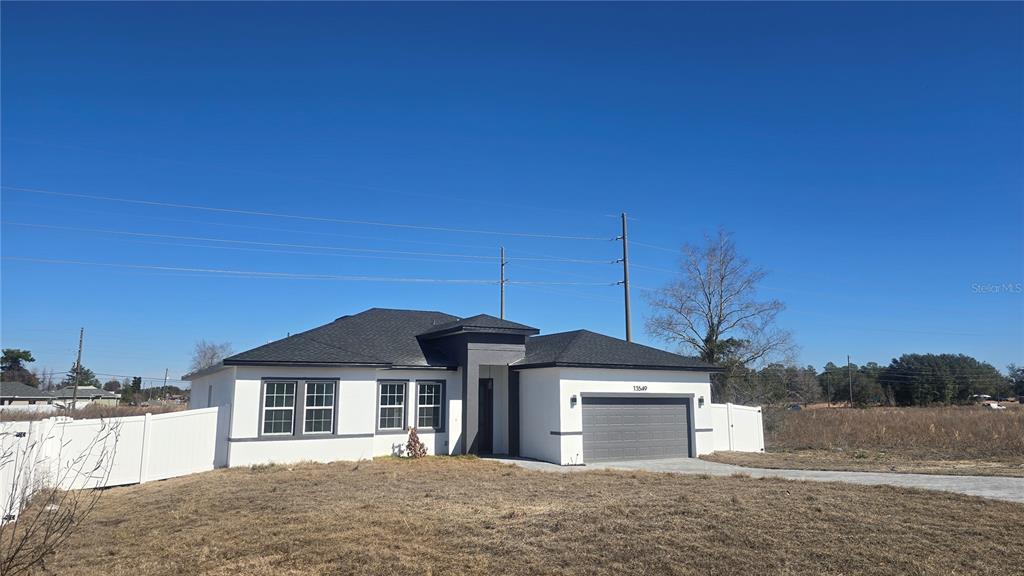 A single-story house with a gray garage, white exterior, and a dark shingled roof — 13549 SW 47TH CIRCLE, OCALA, FL
