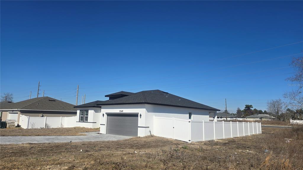A white single-story house with a gray garage door and a white vinyl fence — 13549 SW 47TH CIRCLE, OCALA, FL
