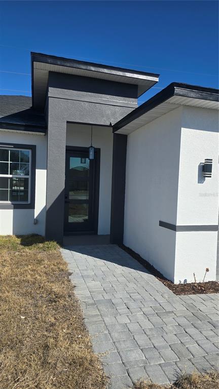 A modern home entrance features a dark gray recessed doorway, white stucco walls, and pavers — 13549 SW 47TH CIRCLE, OCALA, FL