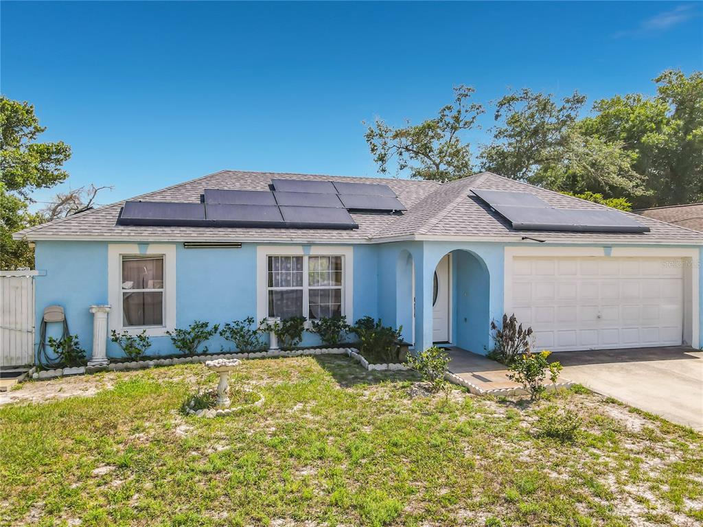 A light blue single-story house features a white garage door and roof-mounted solar panels — 1473 PURITAN STREET, DELTONA, FL