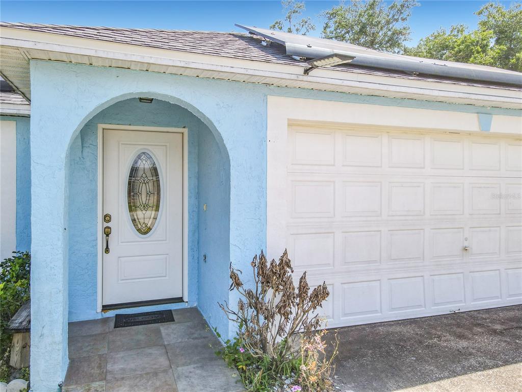 A light blue house exterior features a white front door and a white garage door — 1473 PURITAN STREET, DELTONA, FL