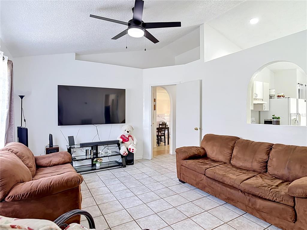 A living room features brown sofas, a wall-mounted television, and tile flooring — 1473 PURITAN STREET, DELTONA, FL