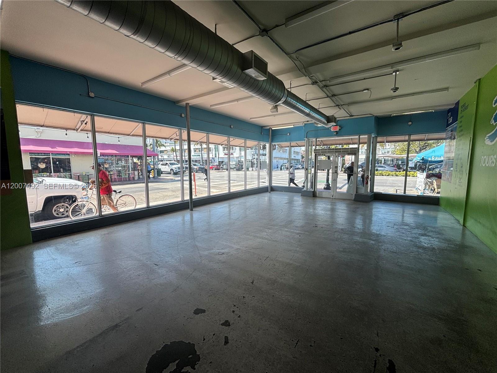 An empty commercial space features concrete floors, exposed ductwork, and large windows facing a street — 1407 Washington Ave # 1401, Miami Beach FL 33139, MIAMI BEACH, FL