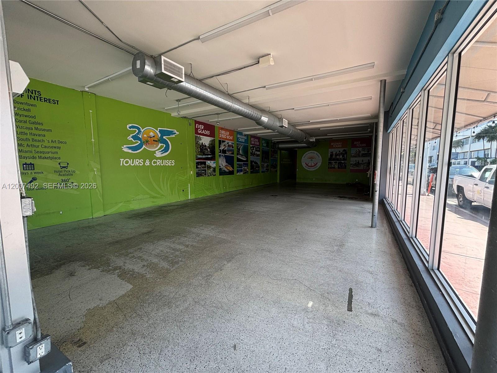 An empty commercial space features a green wall with tour graphics and large windows — 1407 Washington Ave # 1401, Miami Beach FL 33139, MIAMI BEACH, FL