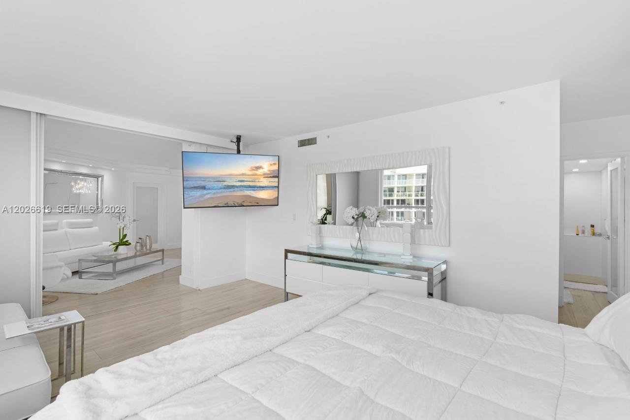 A bedroom features a white bed, a wall-mounted television, and a mirrored console table — 1500 Bay Rd # 1268S, Miami Beach FL 33139, MIAMI BEACH, FL